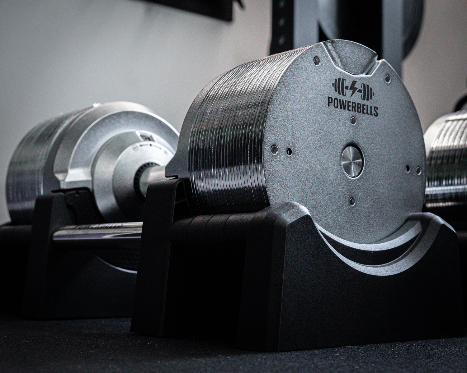 Silver adjustable dumbbell with Powerbells logo resting on black stand.